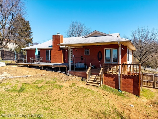 back of property featuring a trampoline, a deck, a chimney, and fence