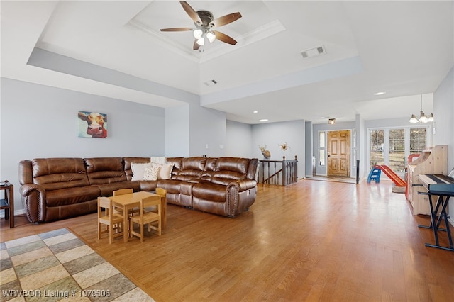 living area with visible vents, a tray ceiling, and wood finished floors