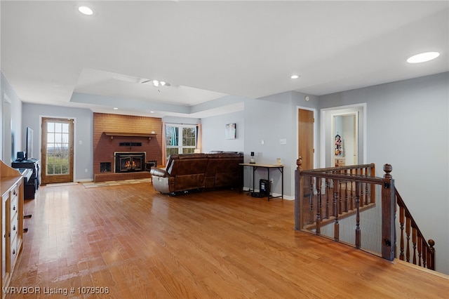 living room featuring a tray ceiling, baseboards, light wood-style floors, and a brick fireplace