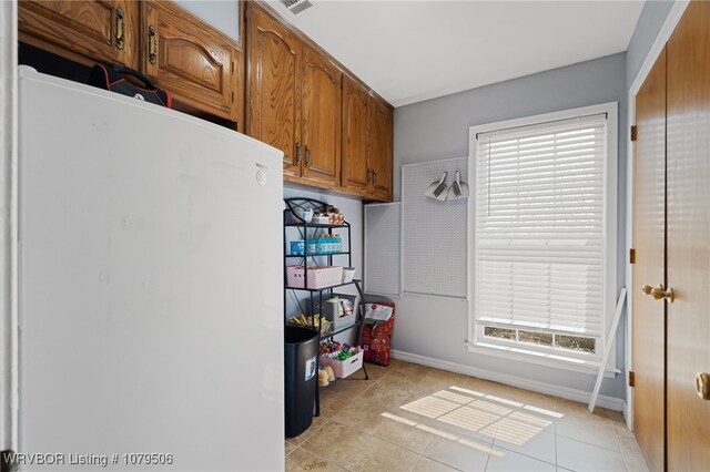 kitchen with visible vents, baseboards, light tile patterned floors, freestanding refrigerator, and brown cabinetry