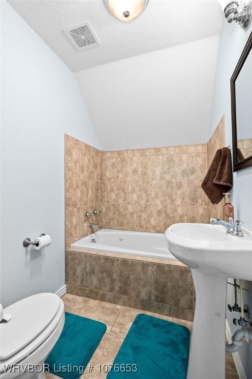 bathroom featuring tile patterned floors, toilet, tiled tub, and vaulted ceiling