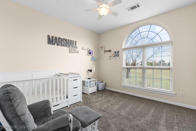 bedroom with ceiling fan, a nursery area, and dark colored carpet