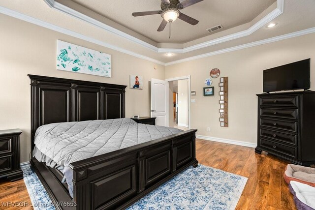 bedroom with hardwood / wood-style floors, ceiling fan, a raised ceiling, and crown molding