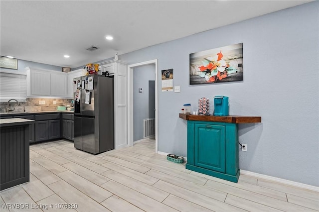 kitchen featuring sink, white cabinetry, gray cabinetry, stainless steel refrigerator with ice dispenser, and tasteful backsplash