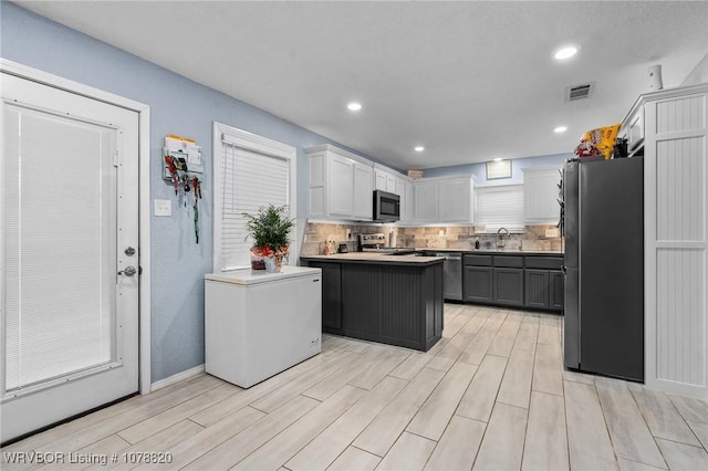 kitchen featuring appliances with stainless steel finishes, white cabinetry, sink, decorative backsplash, and a center island