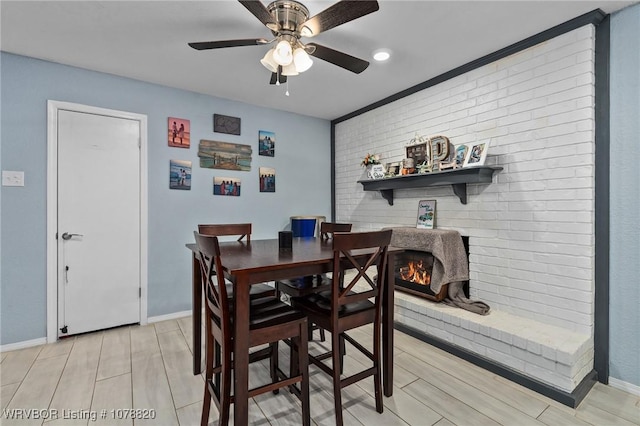 dining area featuring ceiling fan, brick wall, and a brick fireplace