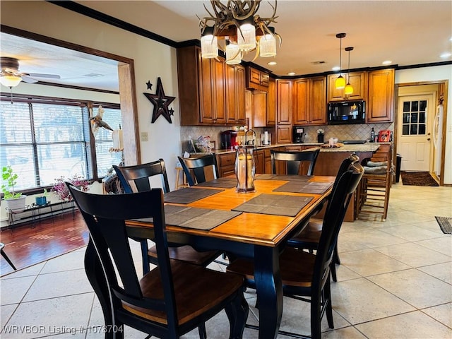 dining space featuring light tile patterned flooring, sink, ornamental molding, and ceiling fan with notable chandelier