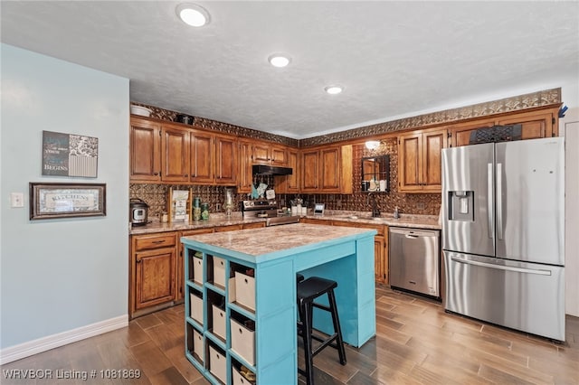 3109 Twin Lakes Pl, Alma, AR 72921 - kitchen with stainless steel appliances, wood finished floors, under cabinet range hood, brown cabinets, and tasteful backsplash