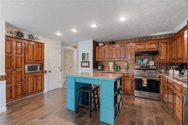 3109 Twin Lakes Pl, Alma, AR 72921 - kitchen featuring stainless steel appliances, a kitchen island, dark wood-type flooring, under cabinet range hood, and brown cabinetry