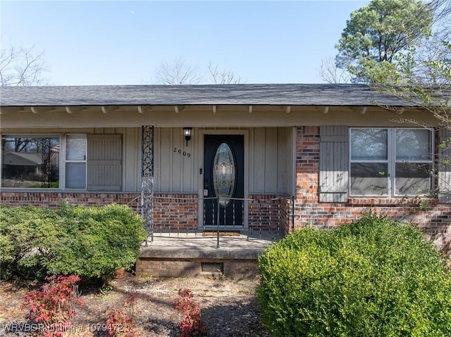 entrance to property featuring board and batten siding, brick siding, a porch, and a shingled roof