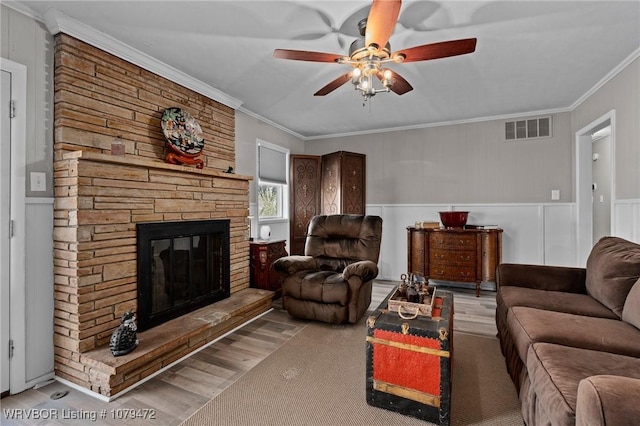 living area with ornamental molding, a fireplace, visible vents, and ceiling fan