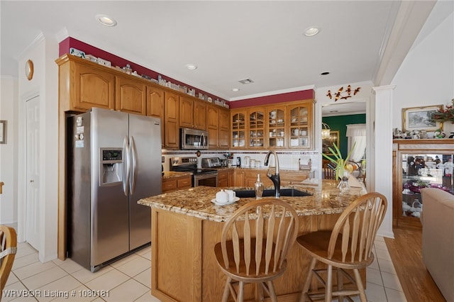 kitchen featuring light stone counters, a sink, crown molding, brown cabinetry, and appliances with stainless steel finishes