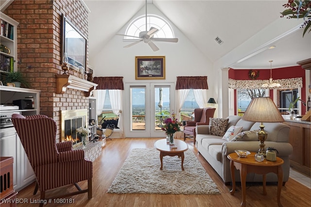 living room with high vaulted ceiling, a ceiling fan, a healthy amount of sunlight, a brick fireplace, and visible vents
