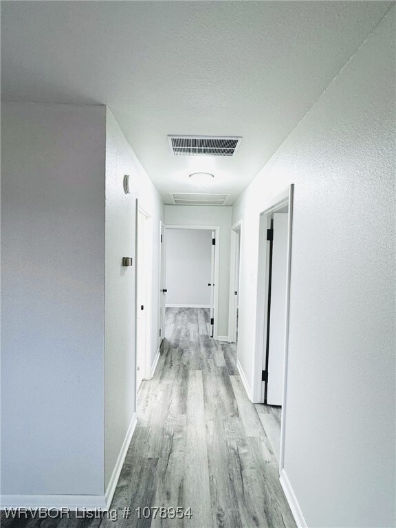 corridor with light wood-type flooring, baseboards, and visible vents