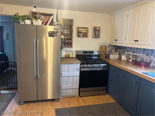 kitchen with wood counters, white cabinets, light wood-type flooring, blue cabinetry, and appliances with stainless steel finishes