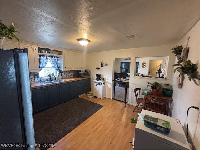 kitchen featuring dishwasher, sink, a textured ceiling, black refrigerator, and light wood-type flooring