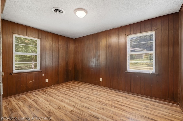 empty room with a textured ceiling, wooden walls, and light hardwood / wood-style flooring