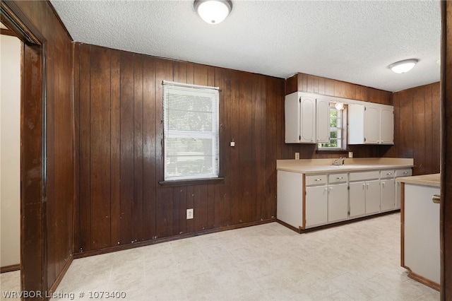 kitchen with a textured ceiling, white cabinetry, wooden walls, and sink