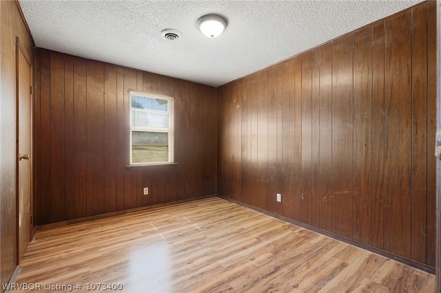 spare room featuring a textured ceiling, wooden walls, and light hardwood / wood-style flooring