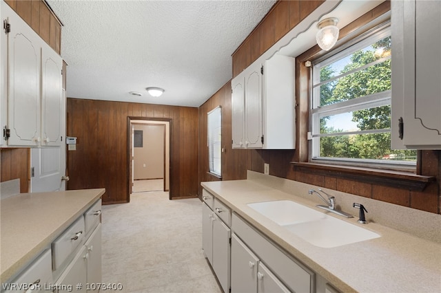 kitchen with white cabinets, wood walls, sink, and a textured ceiling