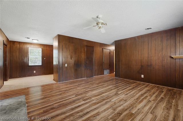 unfurnished room featuring wood walls, ceiling fan, light hardwood / wood-style floors, and a textured ceiling