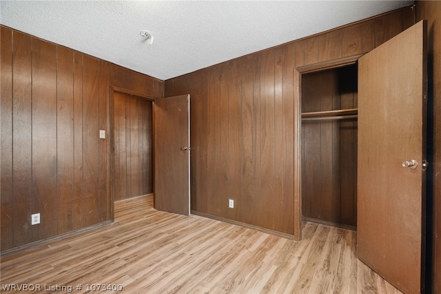 unfurnished bedroom with light wood-type flooring, wooden walls, and a closet