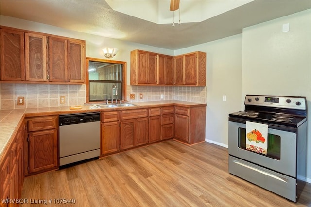 kitchen featuring appliances with stainless steel finishes, ceiling fan, sink, light hardwood / wood-style flooring, and tile counters