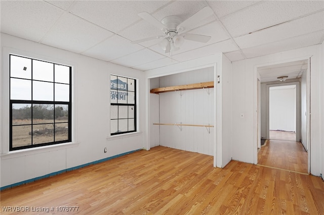 unfurnished bedroom with ceiling fan, a drop ceiling, a closet, and light wood-type flooring