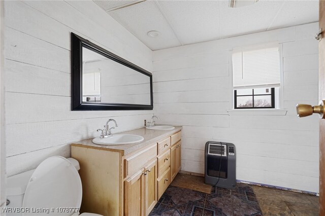 bathroom with heating unit, double vanity, toilet, and a sink