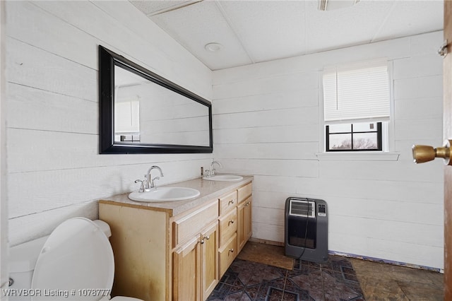 bathroom with heating unit, vanity, toilet, and wood walls