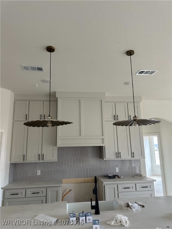 kitchen featuring decorative light fixtures, backsplash, white cabinetry, and visible vents