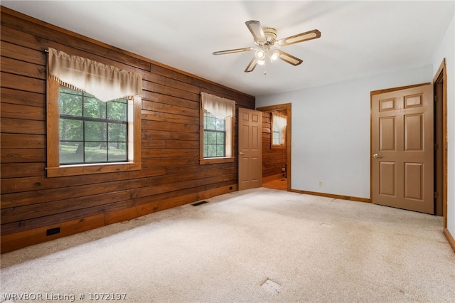 carpeted empty room featuring plenty of natural light, ceiling fan, and wood walls