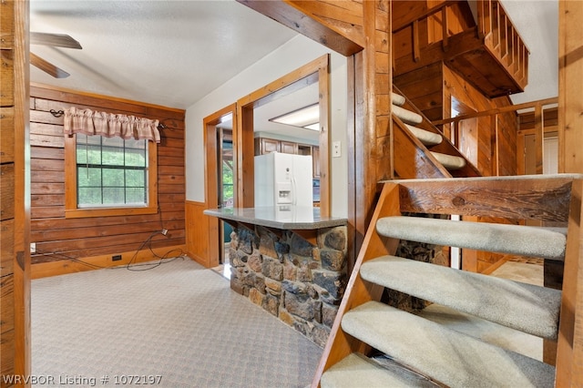 stairway with carpet flooring, wooden walls, and ceiling fan