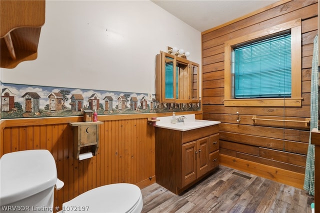 bathroom featuring vanity, toilet, wood-type flooring, and wooden walls