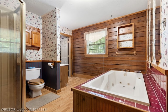 bathroom featuring a bath, toilet, wooden walls, and hardwood / wood-style floors