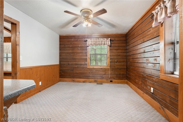 carpeted empty room with wooden walls and ceiling fan