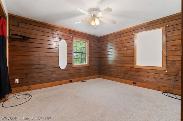 carpeted empty room featuring wood walls and ceiling fan