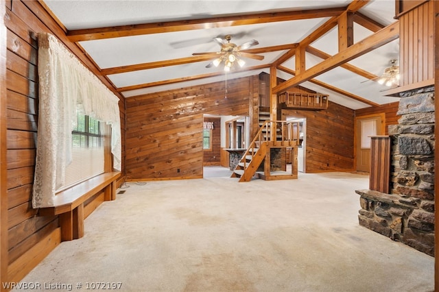 unfurnished living room featuring wood walls, ceiling fan, lofted ceiling with beams, and light colored carpet