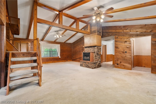 carpeted living room featuring vaulted ceiling with beams, wood walls, a fireplace, and ceiling fan