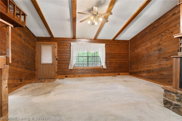 unfurnished living room featuring wooden walls, ceiling fan, lofted ceiling with beams, and light colored carpet