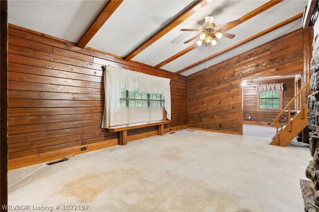 unfurnished living room featuring ceiling fan, a healthy amount of sunlight, and wood walls