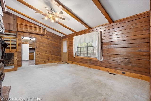 empty room with vaulted ceiling with beams, wood walls, light colored carpet, and ceiling fan