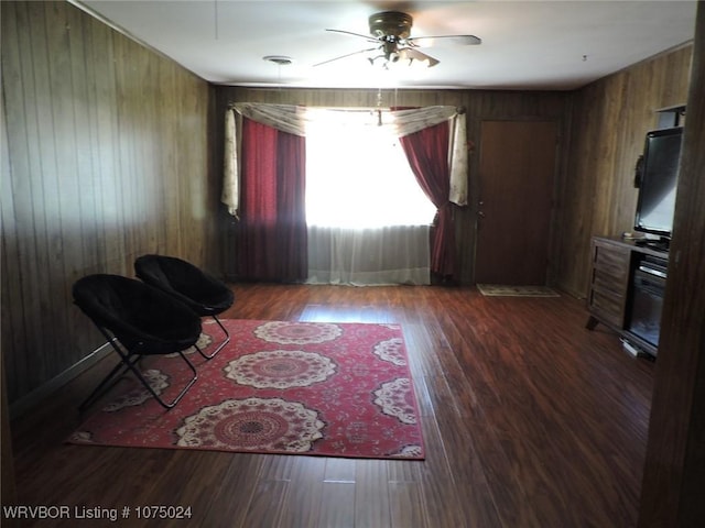 sitting room with wood walls, ceiling fan, and dark hardwood / wood-style floors