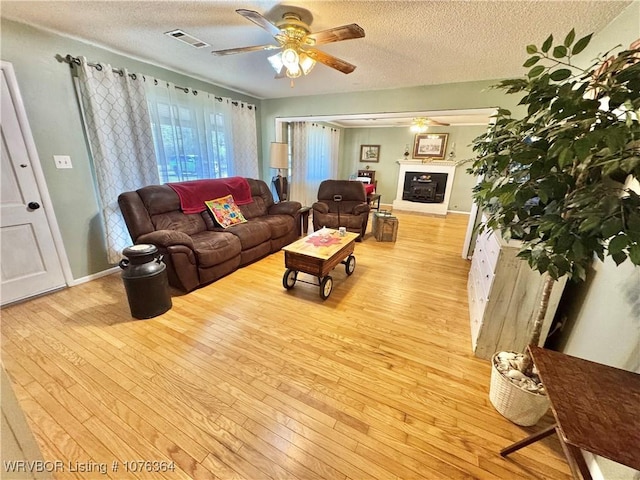 living room with ceiling fan, a textured ceiling, and light wood-type flooring