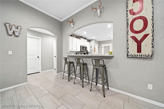 kitchen featuring white cabinets, a kitchen breakfast bar, crown molding, tasteful backsplash, and kitchen peninsula