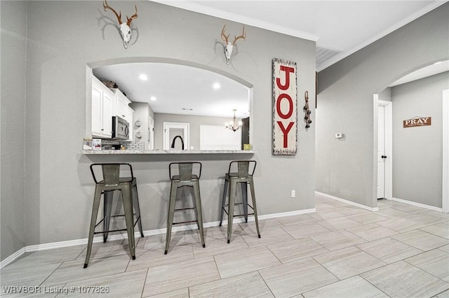 kitchen with a breakfast bar, an inviting chandelier, kitchen peninsula, ornamental molding, and white cabinetry