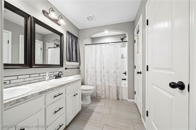 full bathroom featuring tasteful backsplash, a textured ceiling, toilet, shower / tub combo with curtain, and vanity