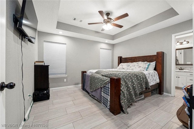 bedroom with a tray ceiling, connected bathroom, ceiling fan, and sink