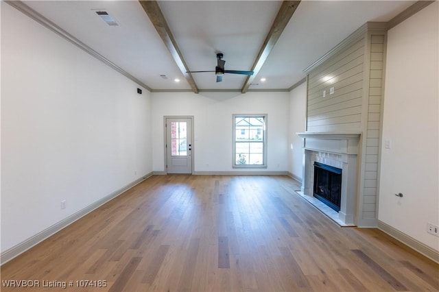 unfurnished living room with ornamental molding, ceiling fan, beam ceiling, a fireplace, and light hardwood / wood-style floors