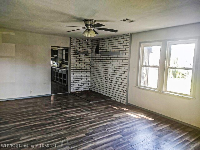 unfurnished room with dark wood-style floors, visible vents, ceiling fan, and baseboards